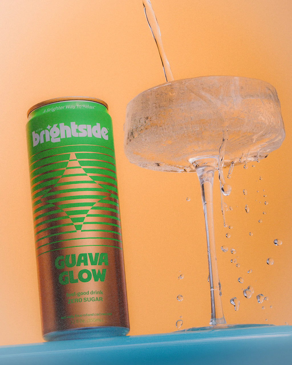 A can of Brightside Guava Glow soda stands next to a coupe glass with it being poured, set against a solid orange background.