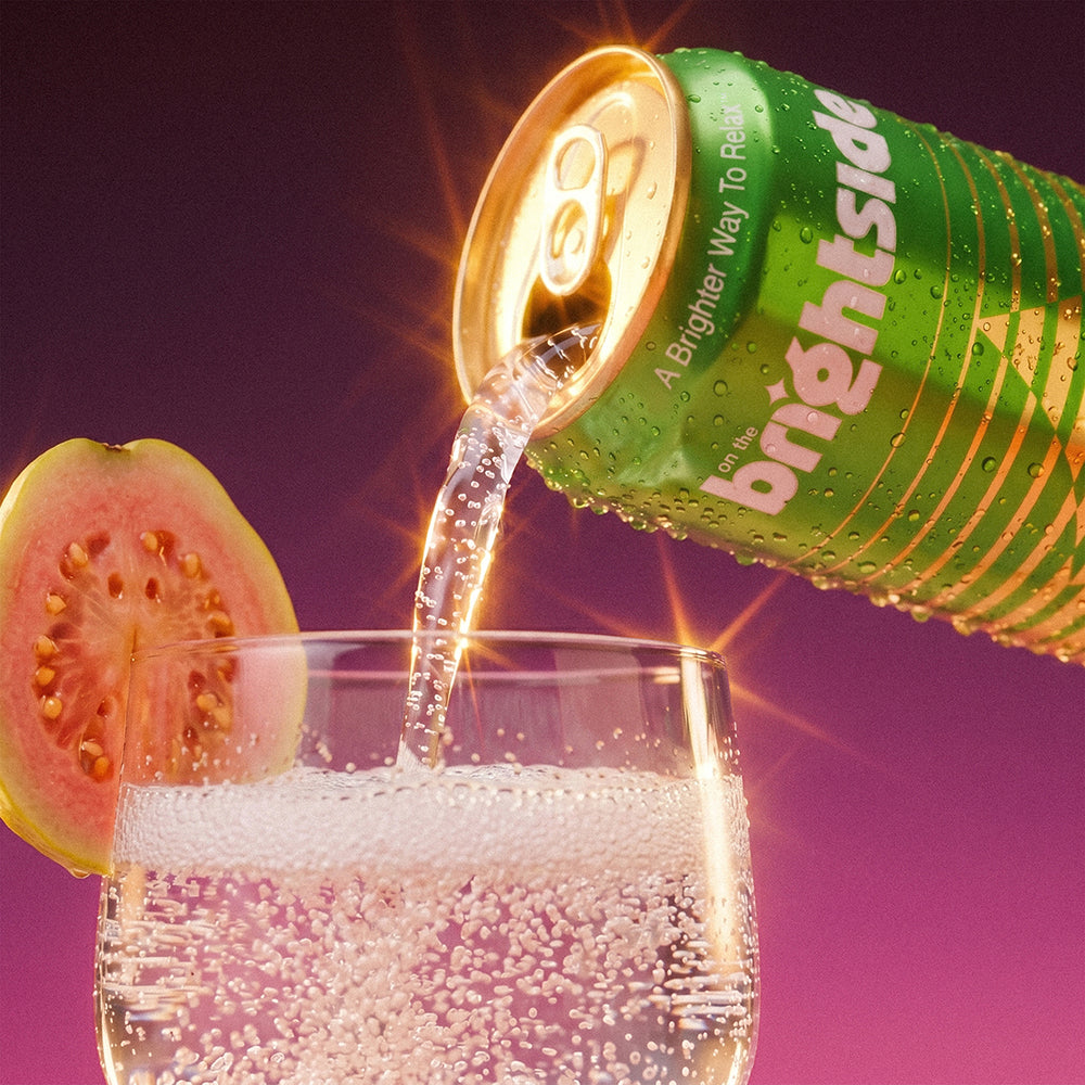 Guava Glow On the Brightside beverage can tilted to pour a clear bubbly drink into a glass, with a pink guava slice on the rim, against a purple gradient background with bright light effects.