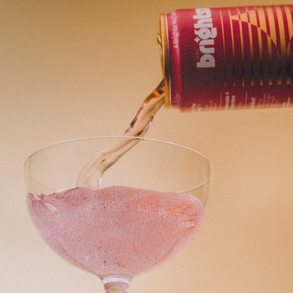 Strawberry Sunshine On the Brightside soft drink being poured into a clear glass, creating a pinkish liquid splash against a warm beige background.