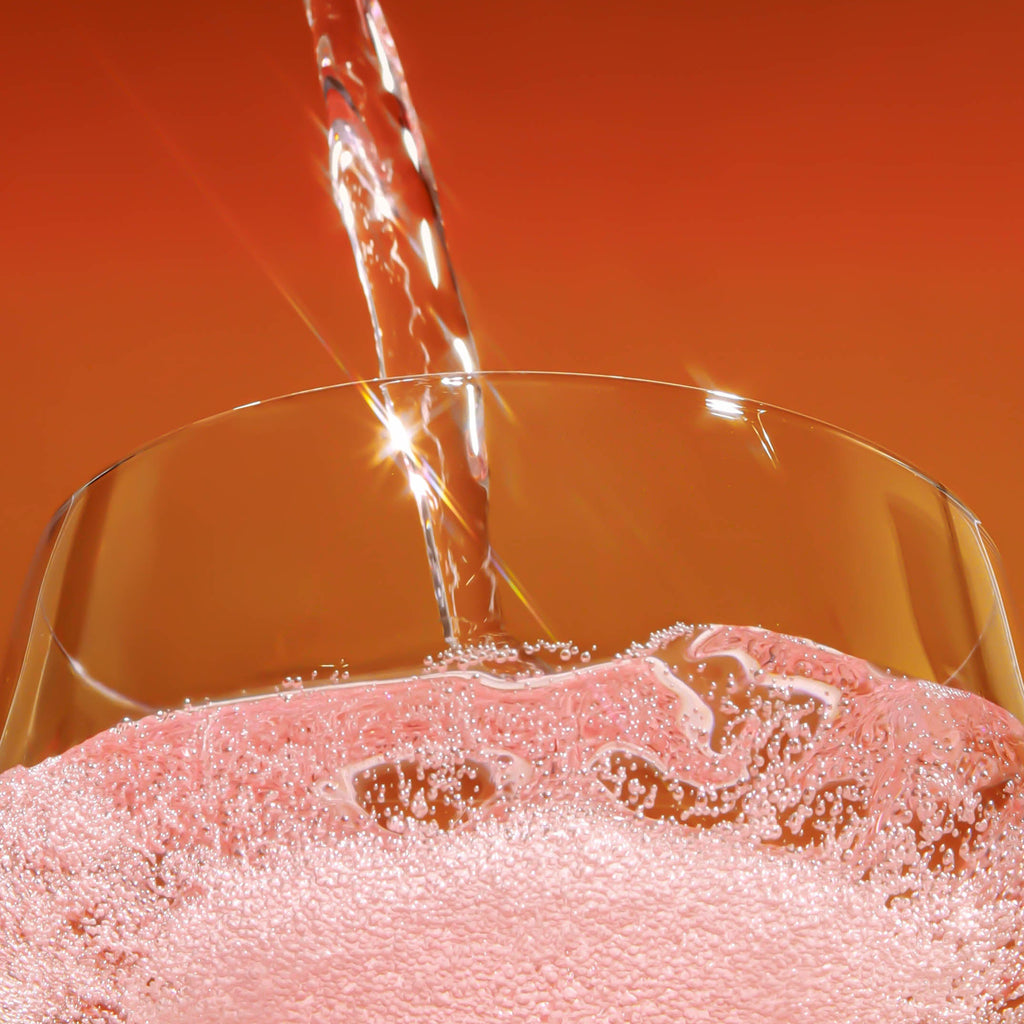 brightside strawberry sunshine being poured into a clear glass against a warm orange gradient background.
