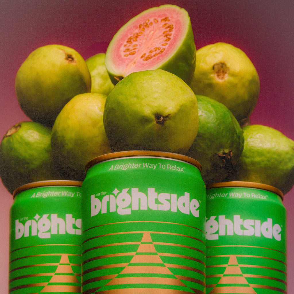Three green On the Brightside Guava Glow cans with guava slices on a pink background