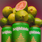 Three green On the Brightside Guava Glow cans with guava slices on a pink background